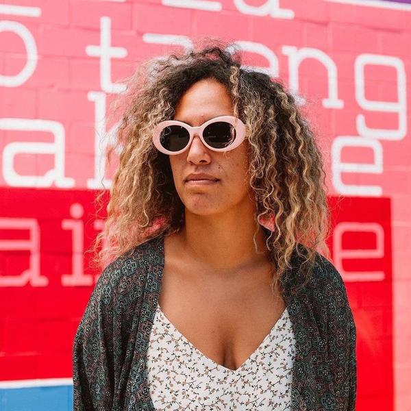 A person wearing pink sunglasses standing against a pink and red painted background